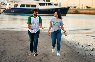 young man and woman walking on beach are near campus